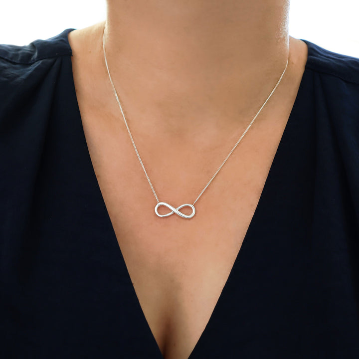 Infinity symbol sterling 925 silver necklace worn by a woman in a dark blue silk blouse