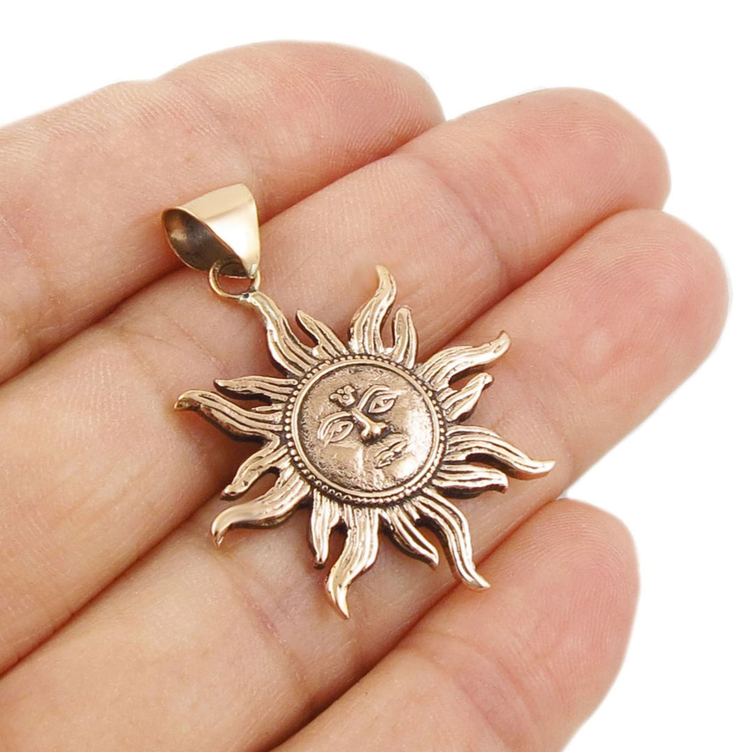 Copper sun-shaped pendant held in a hand against a white background
