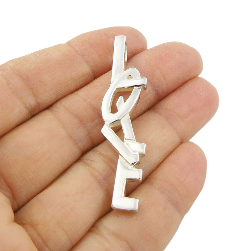 Silver pendant shaped like the word 'LOVE' held in a hand against a white background