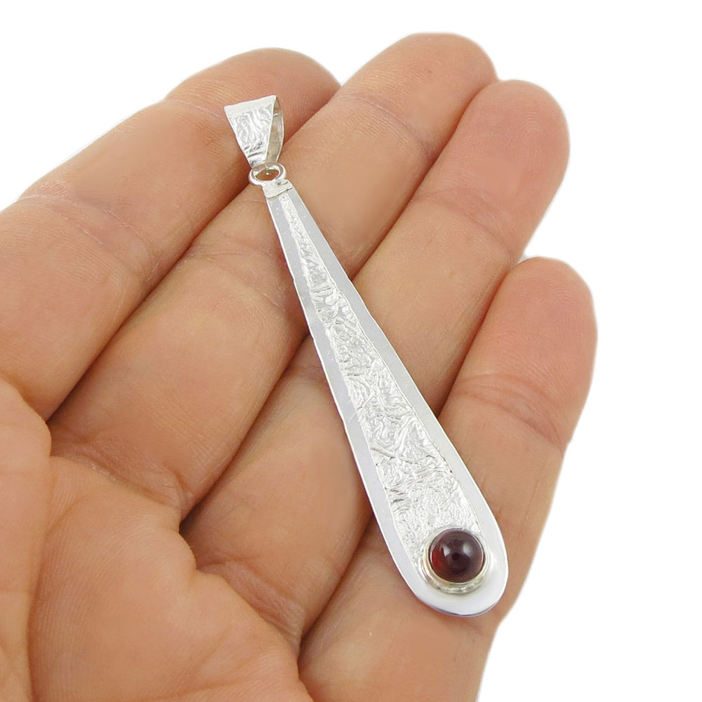 Long Taxco, Mexico 925 silver pendant jewellery with a red natural garnet gemstone held between fingers on a white background