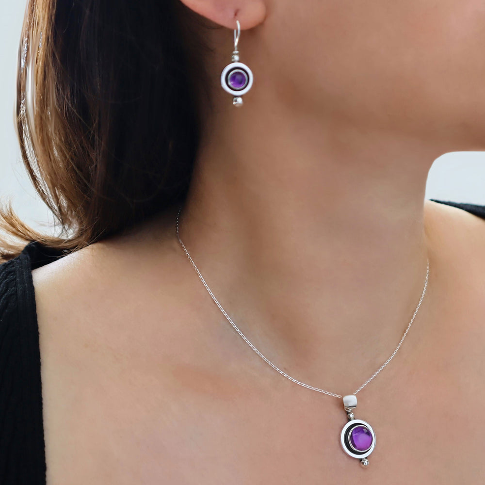 Close-up of a woman wearing a silver necklace with a purple amethyst gemstone and matching earrings.