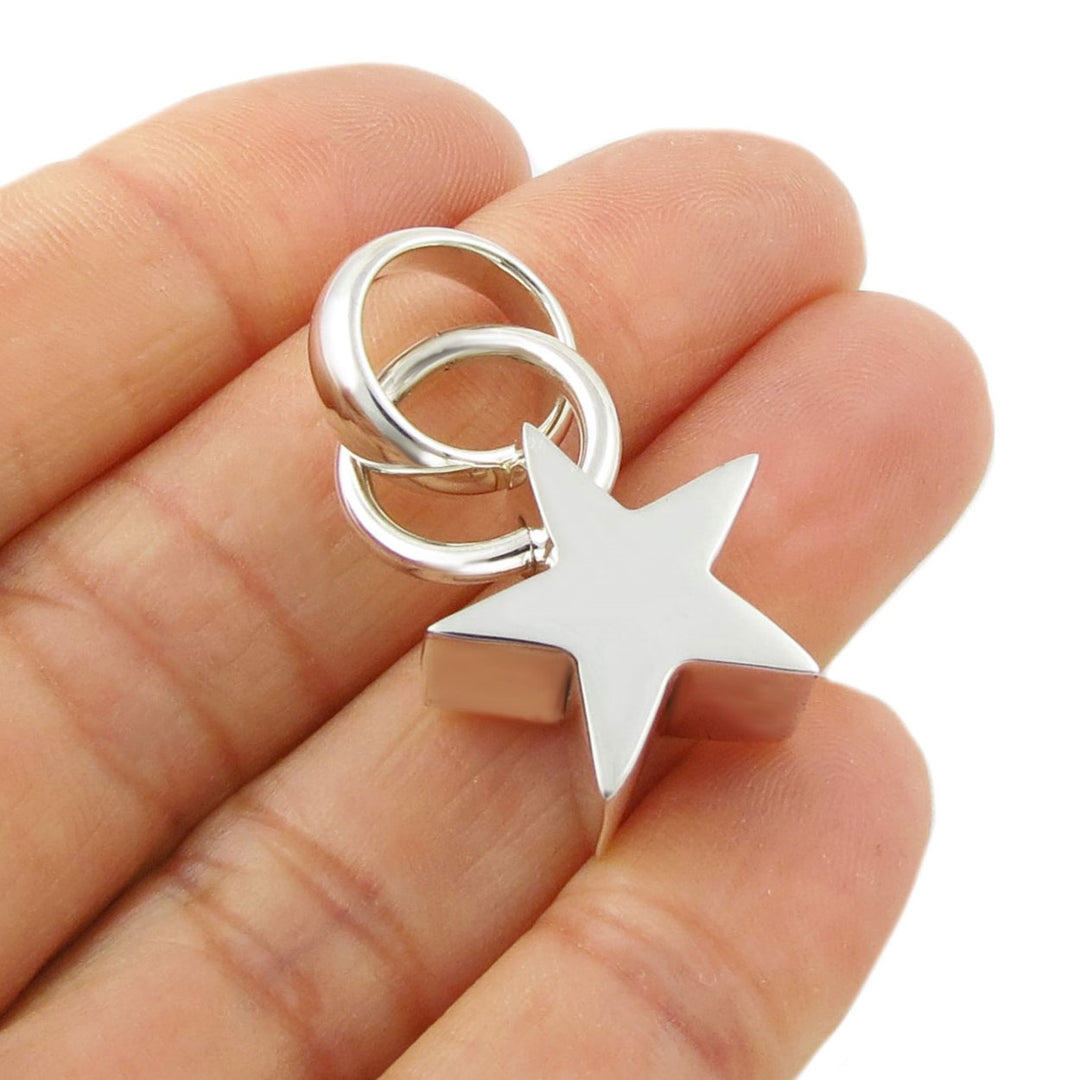 Silver star-shaped pendant held between fingers on a white background