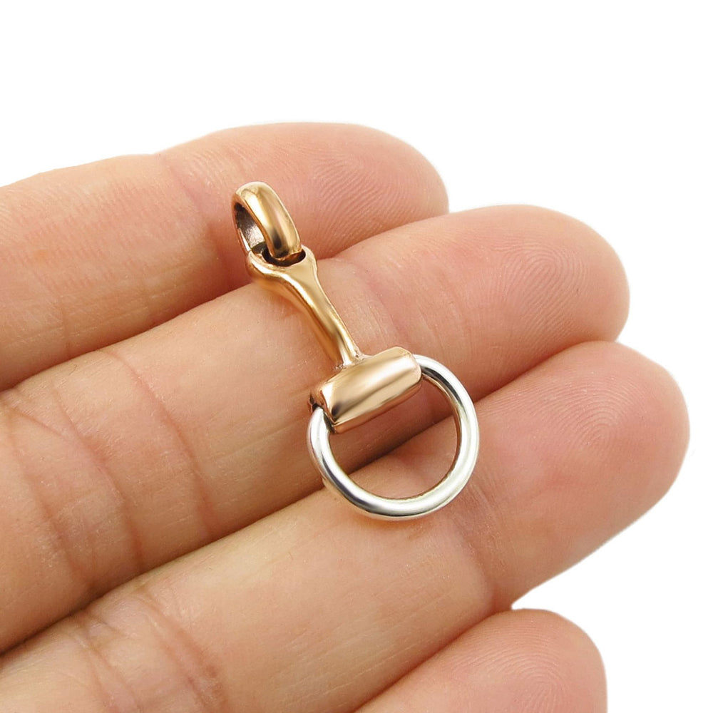 Copper and silver horse bit pendant held between fingers on a white background