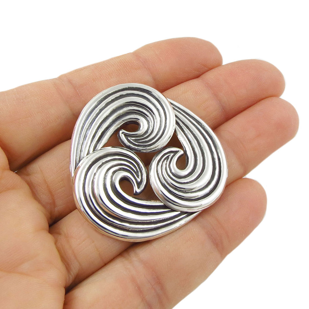 Large silver pendant with a wave design held in a hand against a white background