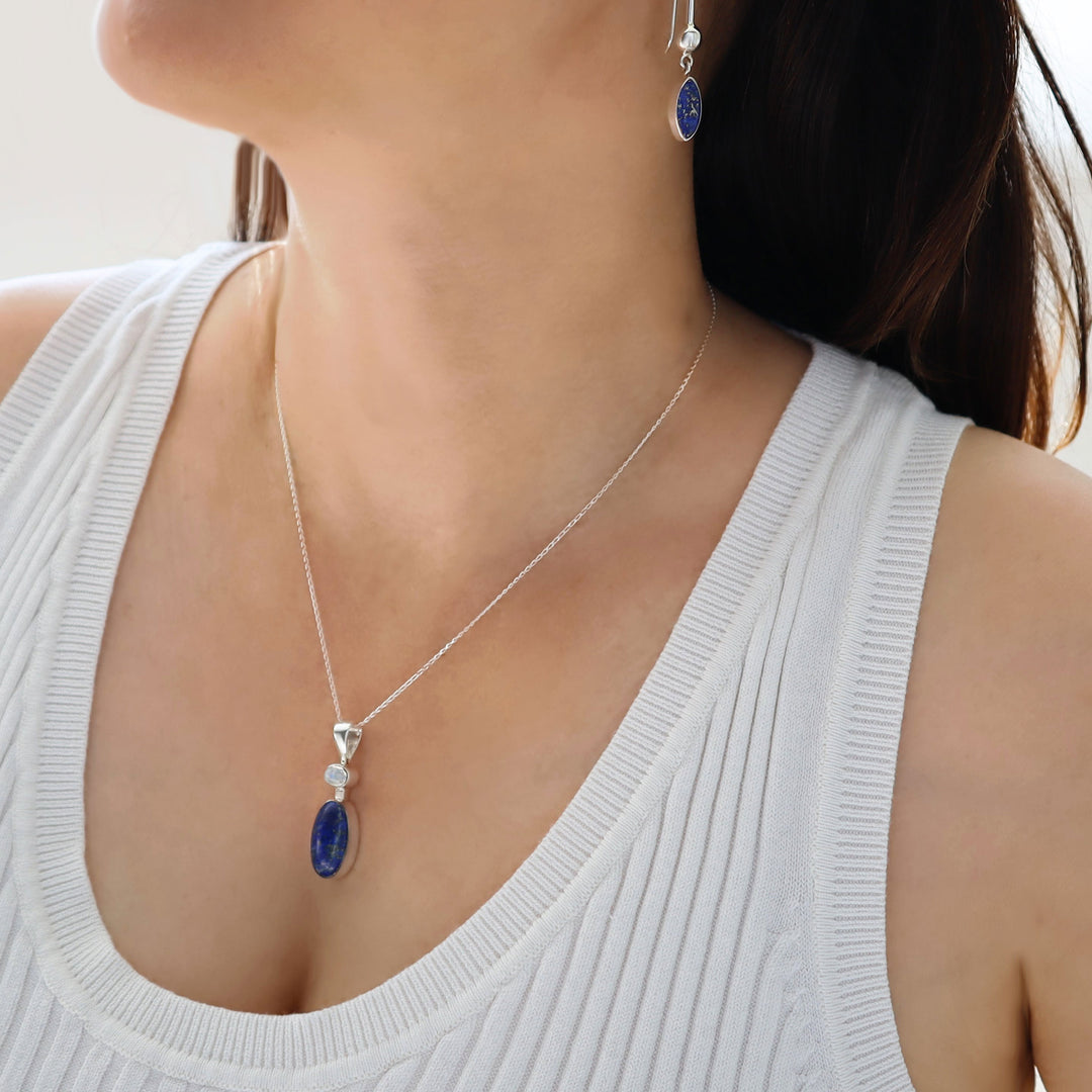 A woman in a white top wearing a blue lapis lazuli pendant necklace and matching earrings. 