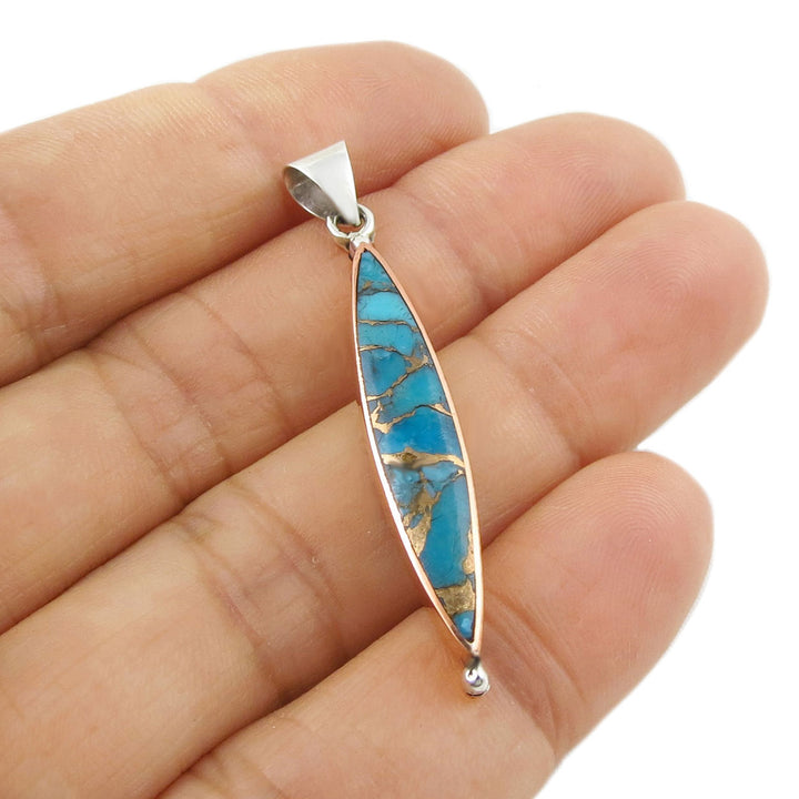 Turquoise pendant with silver setting held between fingers on a white background