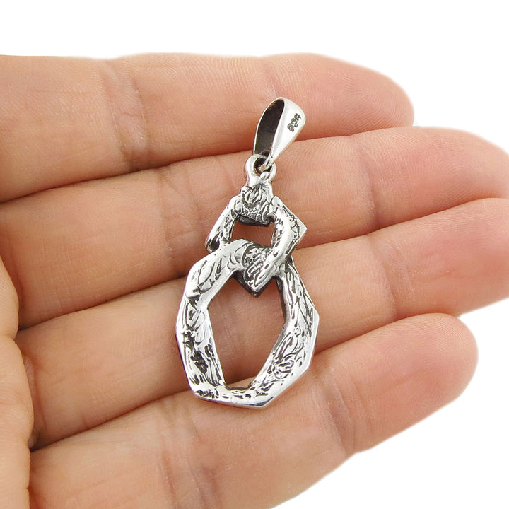 Silver pendant held upside down to reveal the 925 hallmark in a hand against a white background