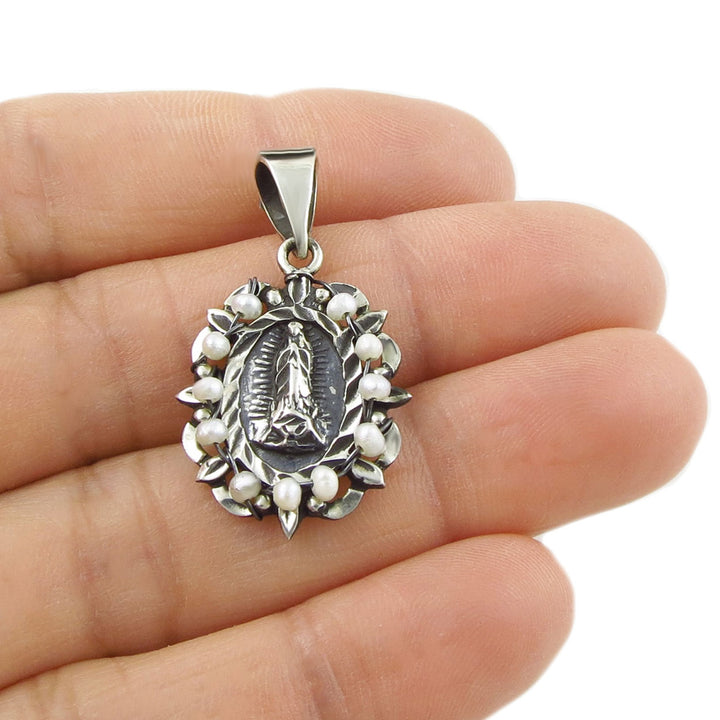 Hand holding a Baroque 925 silver pendant with an image of the Virgin Mary surrounded by seed pearls with a polished and blackened antiqued finish