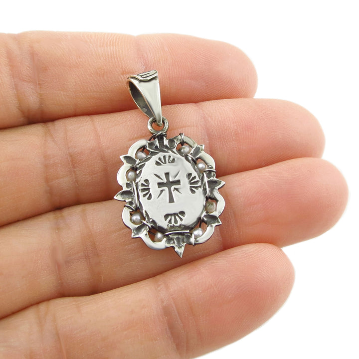 Reverse of a 925 silver pendant engraved with a religious cros held between fingers against a white background