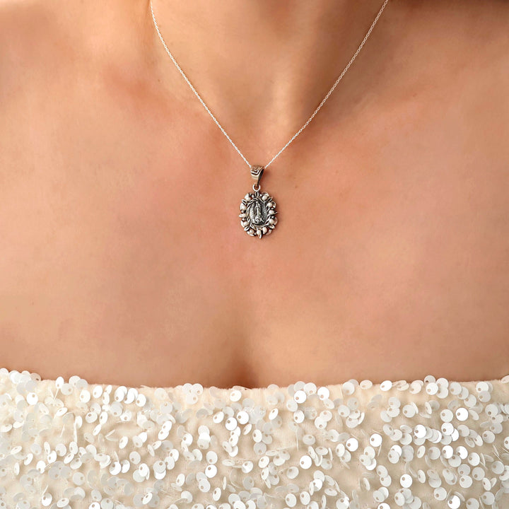Woman in a sequinned top wearing a Baroque 925 sterling silver pendant and chain necklace featuring the Virgin Mary surrounded by seeds pearls