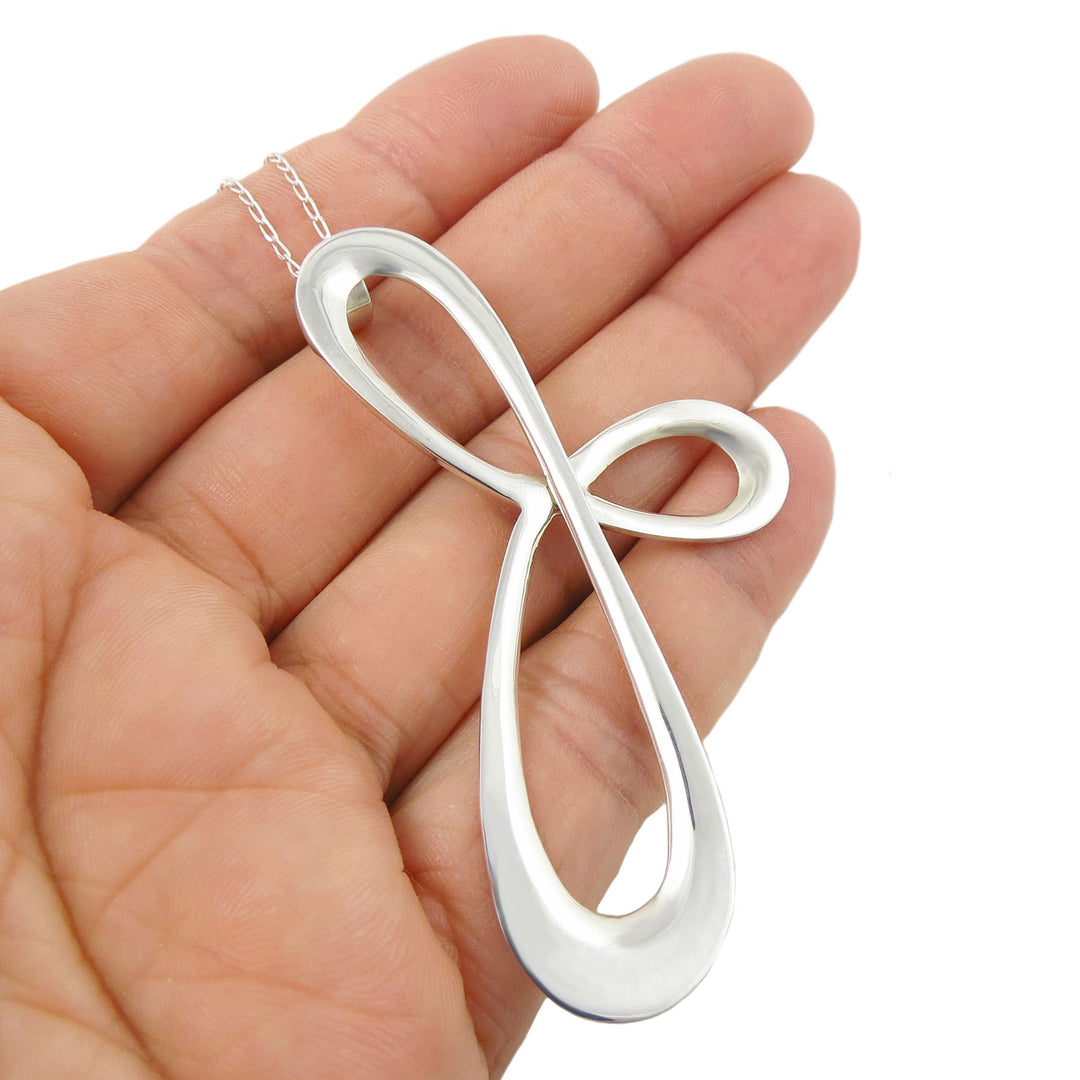 A large handmade infinity spiral pendant in sterling silver held in a person's hand