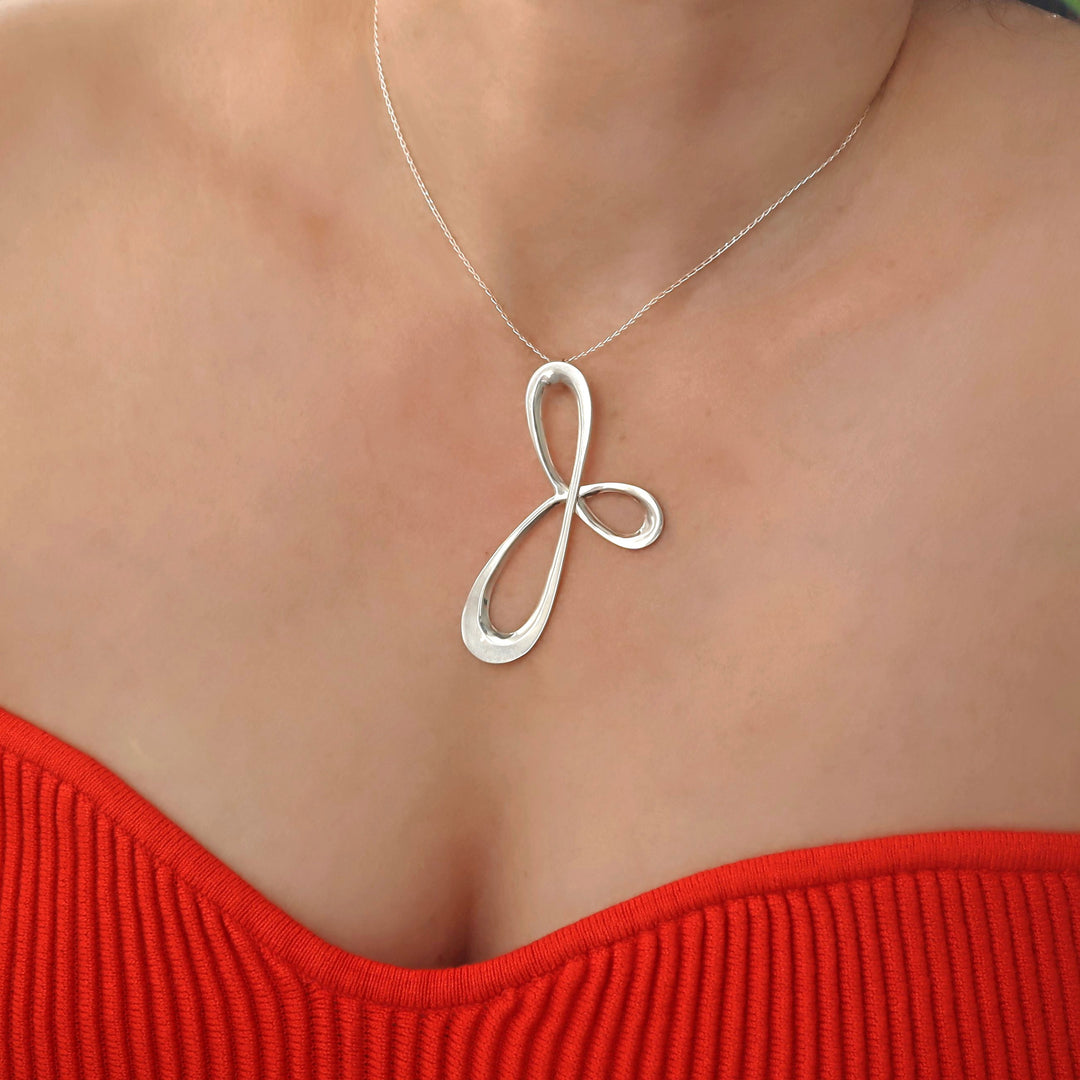 A woman wearing a red top with a large three pointed infinity spiral pendant hanging on a chain handmade from sterling silver