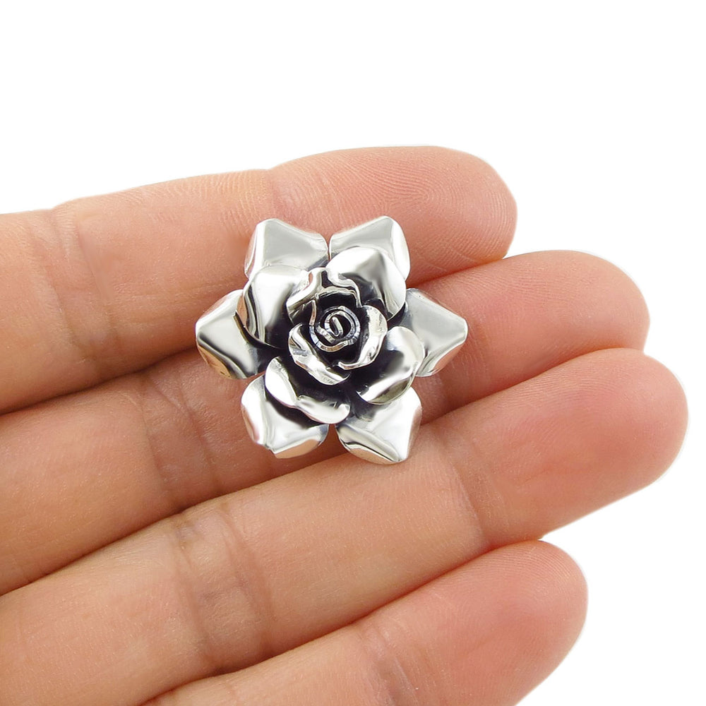Taxco 925 sterling silver rose-shaped pendant jewellery held between fingers on a white background
