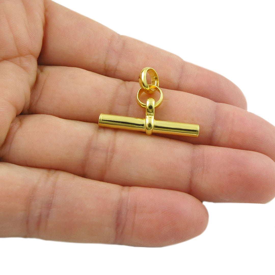 Yellow gold chunky t-bar pendant held between fingers on a white background