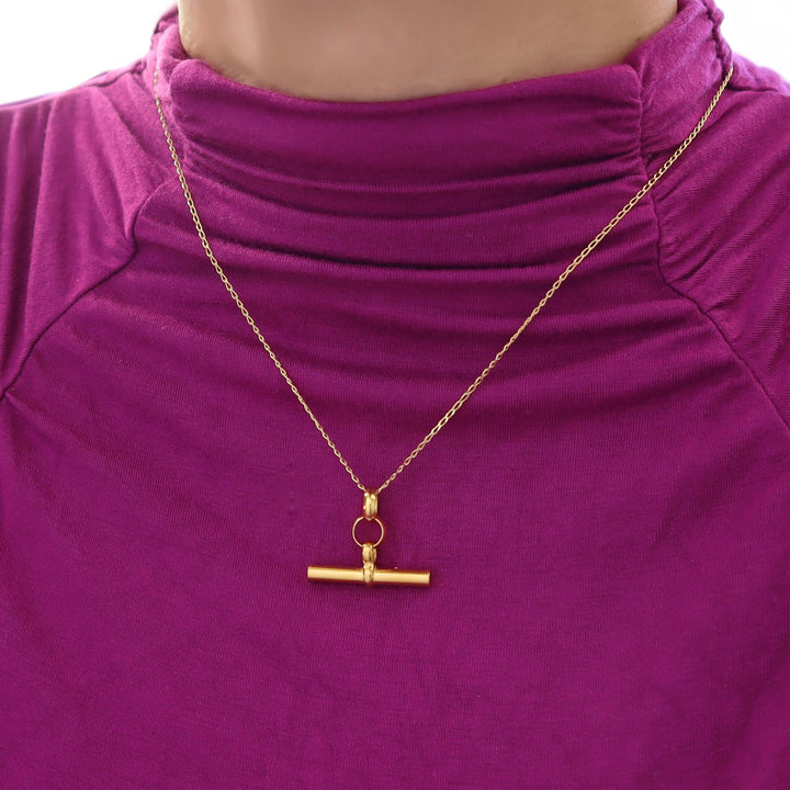 Gold t-bar chain necklace with a pendant on a purple turtleneck top