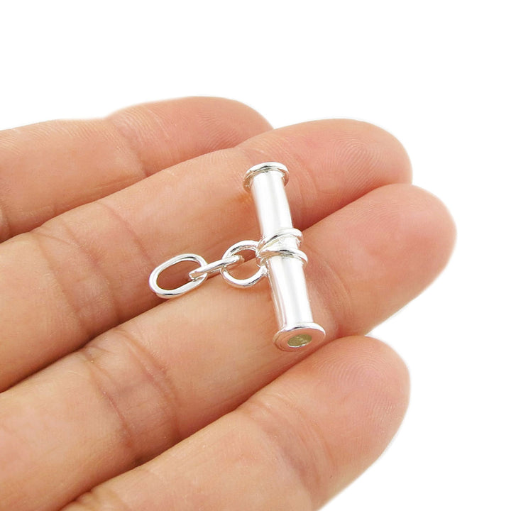 A sterling silver albert t-bar pendant jewellery held in a hand on a white background. 