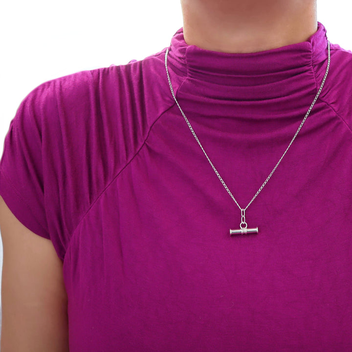 A medium sized 925 ilver t bar pendant and curb chain necklace worn by a woman in a purple top