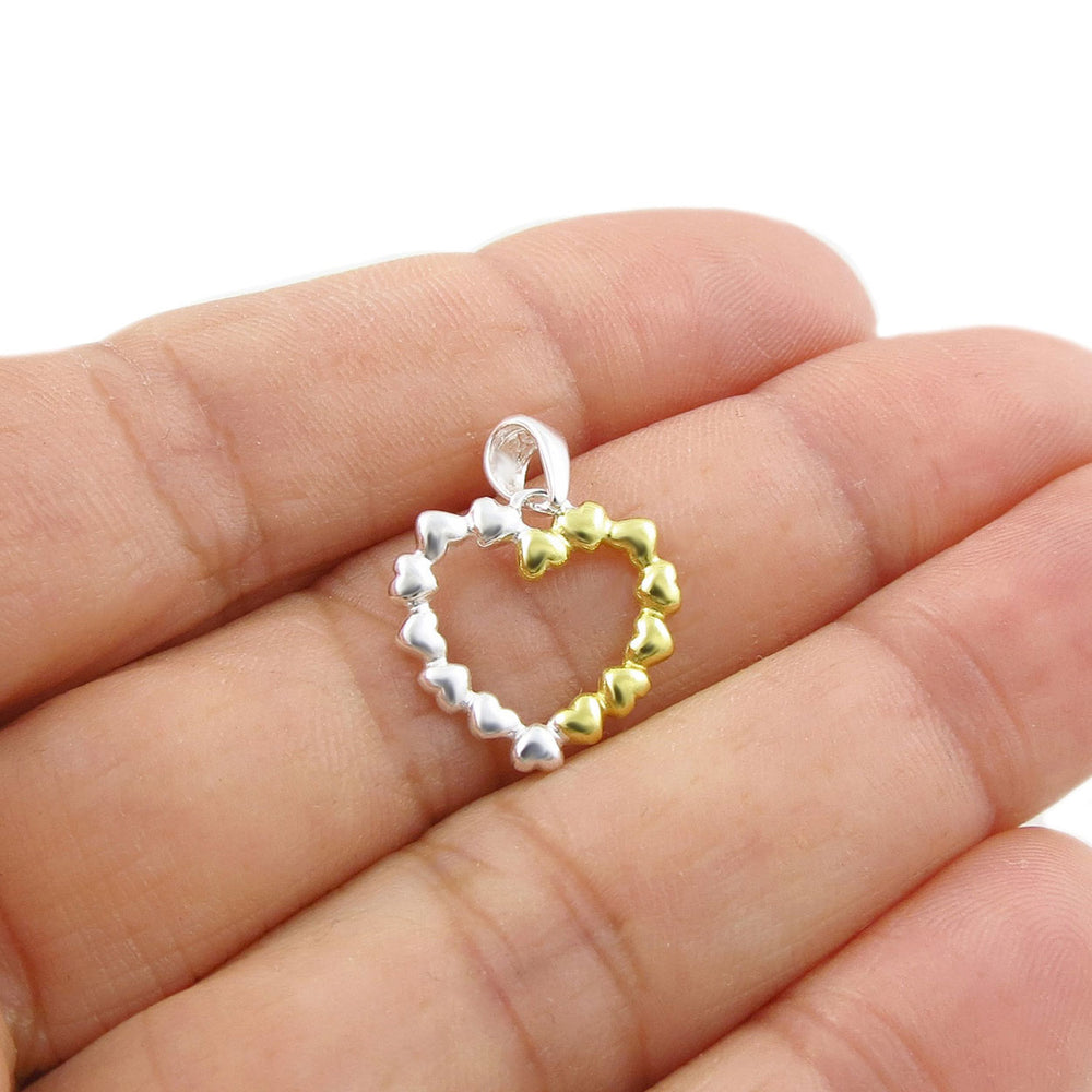  A heart-shaped pendant in 925 silver with yellow gold accents held between fingers on a white background