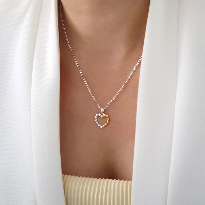 925 silver chain and heart shaped pendant necklace with yellow gold accents worn by a woman with a white jacket
