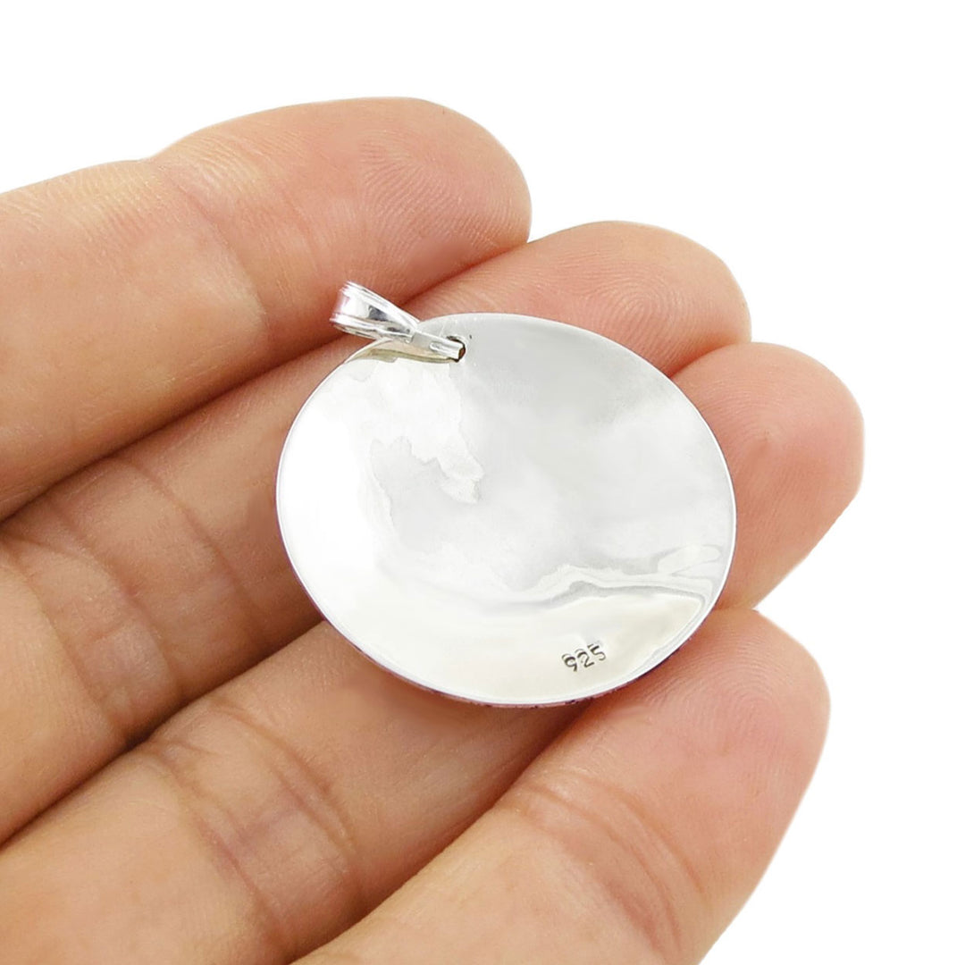 Reverse of round 925 silver pendant showing it stamped 925 held between fingers on a white background