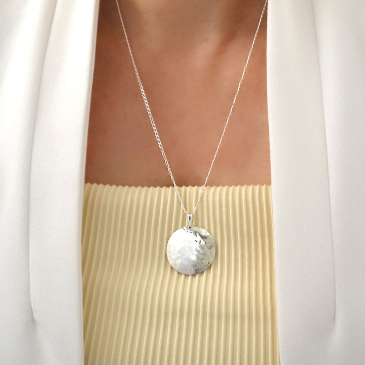 Large hammered Mexican 925 sterling silver pendant and silver curb chain necklace worn by a woman in a white jacket.