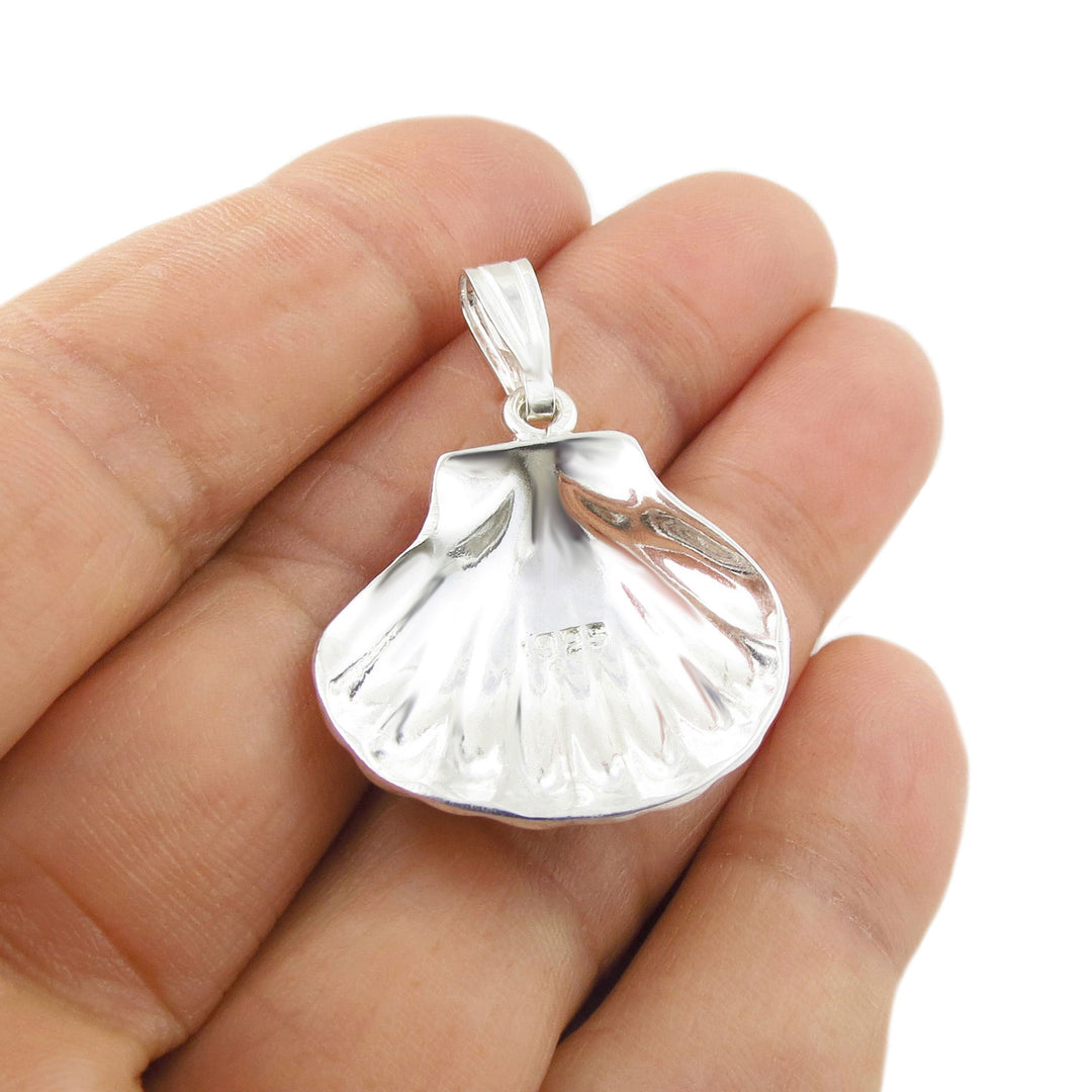 Sterling Silver sea shell pendant held upsside down in a hand to reveal the 925 hallmark against a white background
