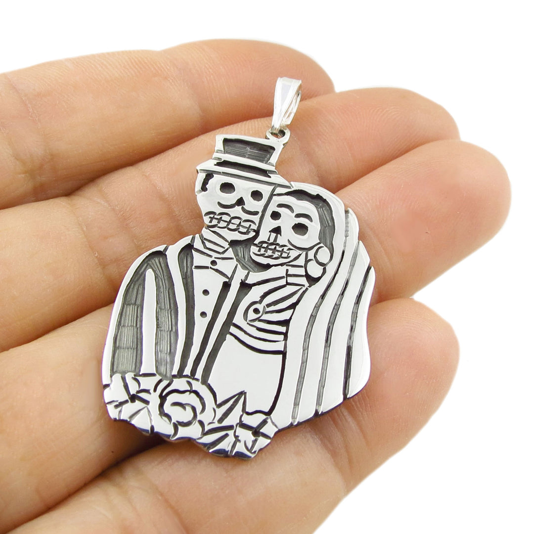 Mexican 925 silver bride and groom calavera skeleton couple pendant jewellery held in a hand against a white background