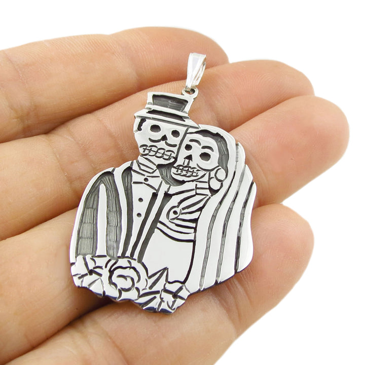 Mexican 925 silver bride and groom calavera skeleton couple pendant jewellery held in a hand against a white background