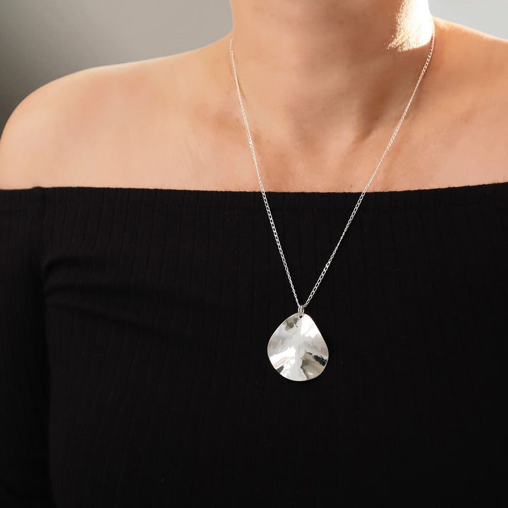 Long 925 sterlling Silver necklace with a hammered pendant worn by a woman against a neutral background