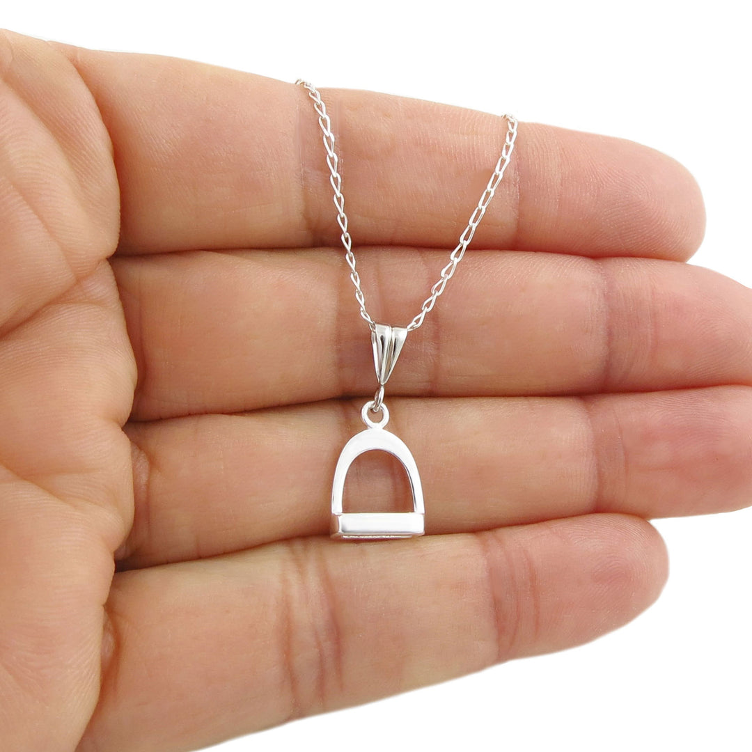 A sterling 925 sillver equetrian design horse stirrup pendant and curb link chain necklace held in a person'd hand 