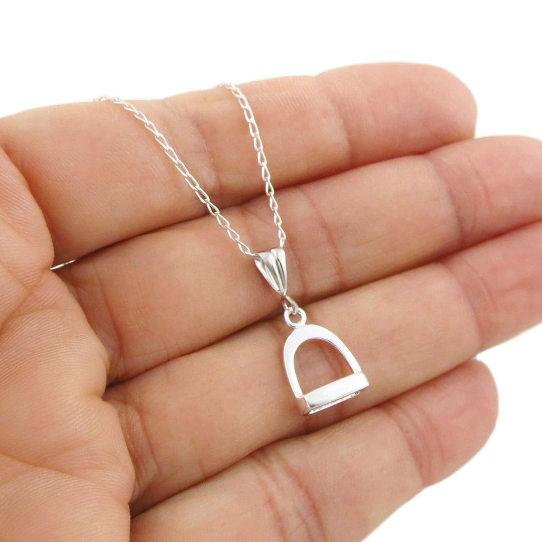 A small sterling silver hore stirrup pendant and chain necklace for women held in a persons hand