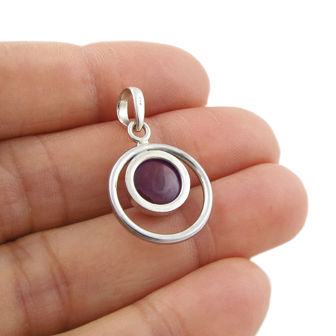Sterling 925 Silver pendant with a purple amethyst February birthstone gemstone held between fingers on a white background