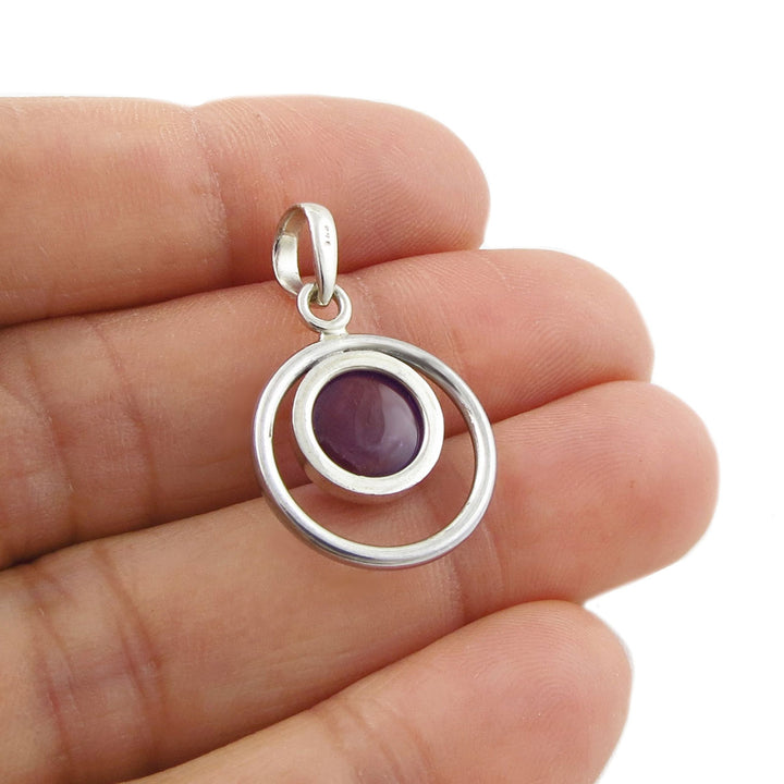 Sterling 925 Silver pendant with a purple amethyst February birthstone gemstone held between fingers on a white background