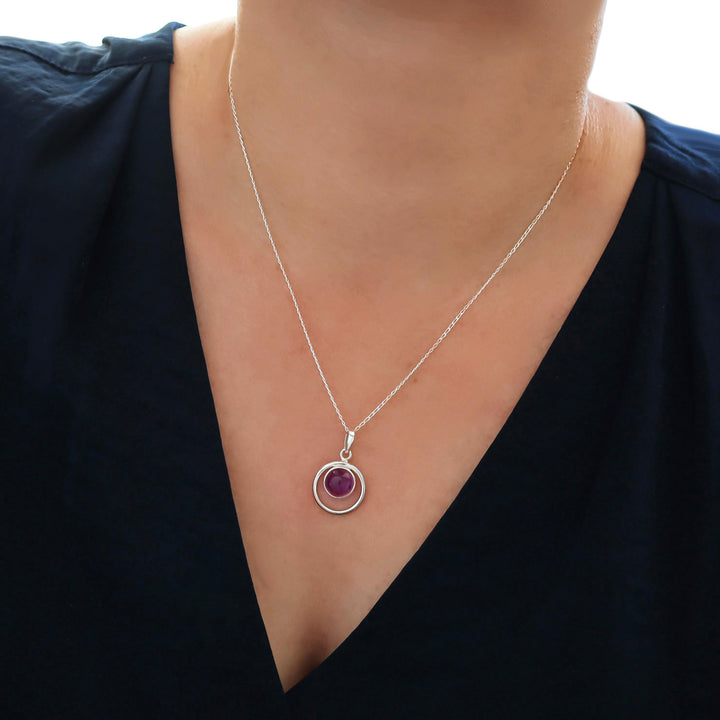 A 925 sterling silver pendant and chain necklace with an amethyst birthstone worn by a woman in a blue silk blouse
