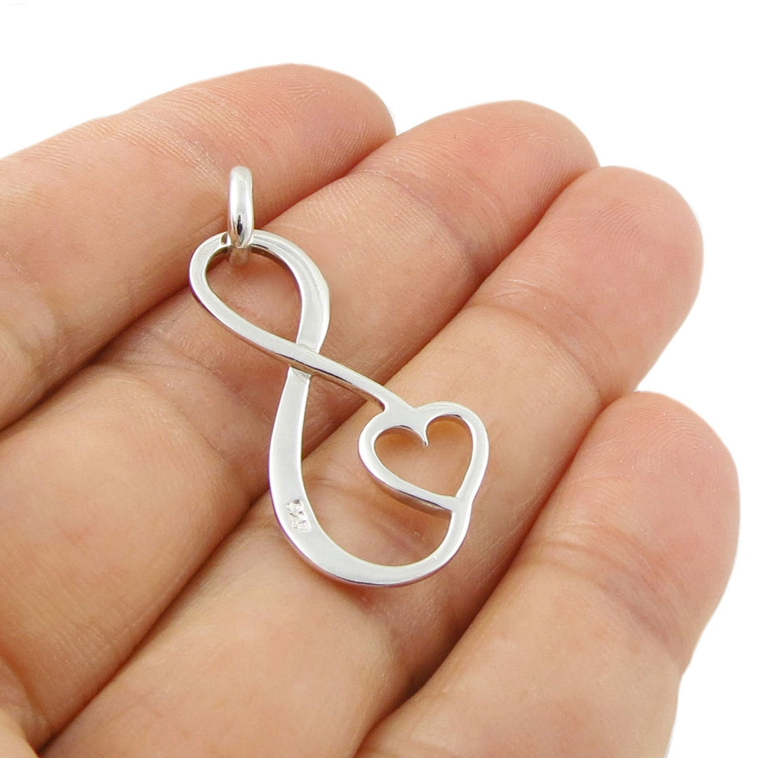 A large terling 925 silver figure of eight with love heart pendant held in a woman's hand