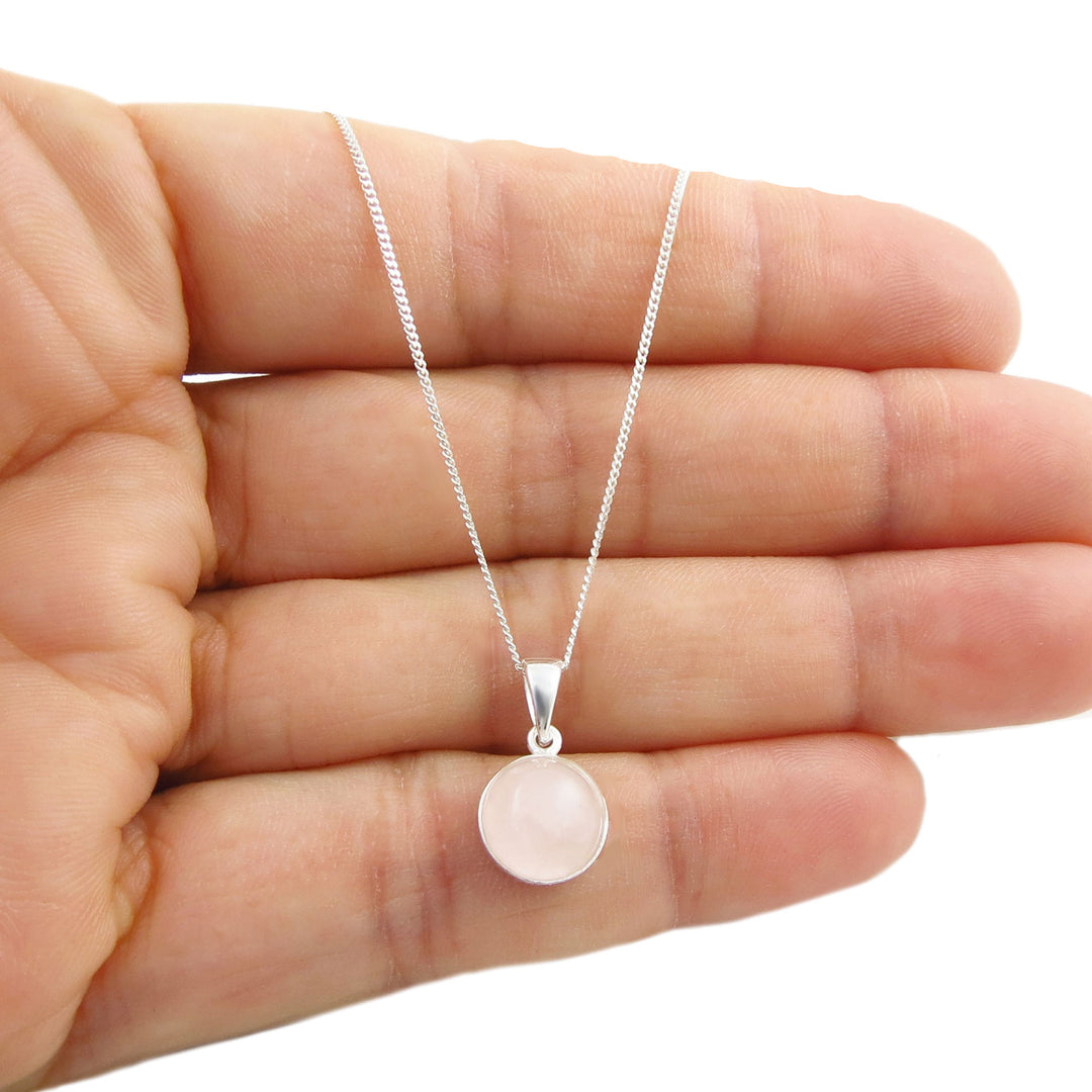 A 925 sterling silver necklace with a round pale pink rose quartz stone pendant, held in the palm of a hand against a white background.