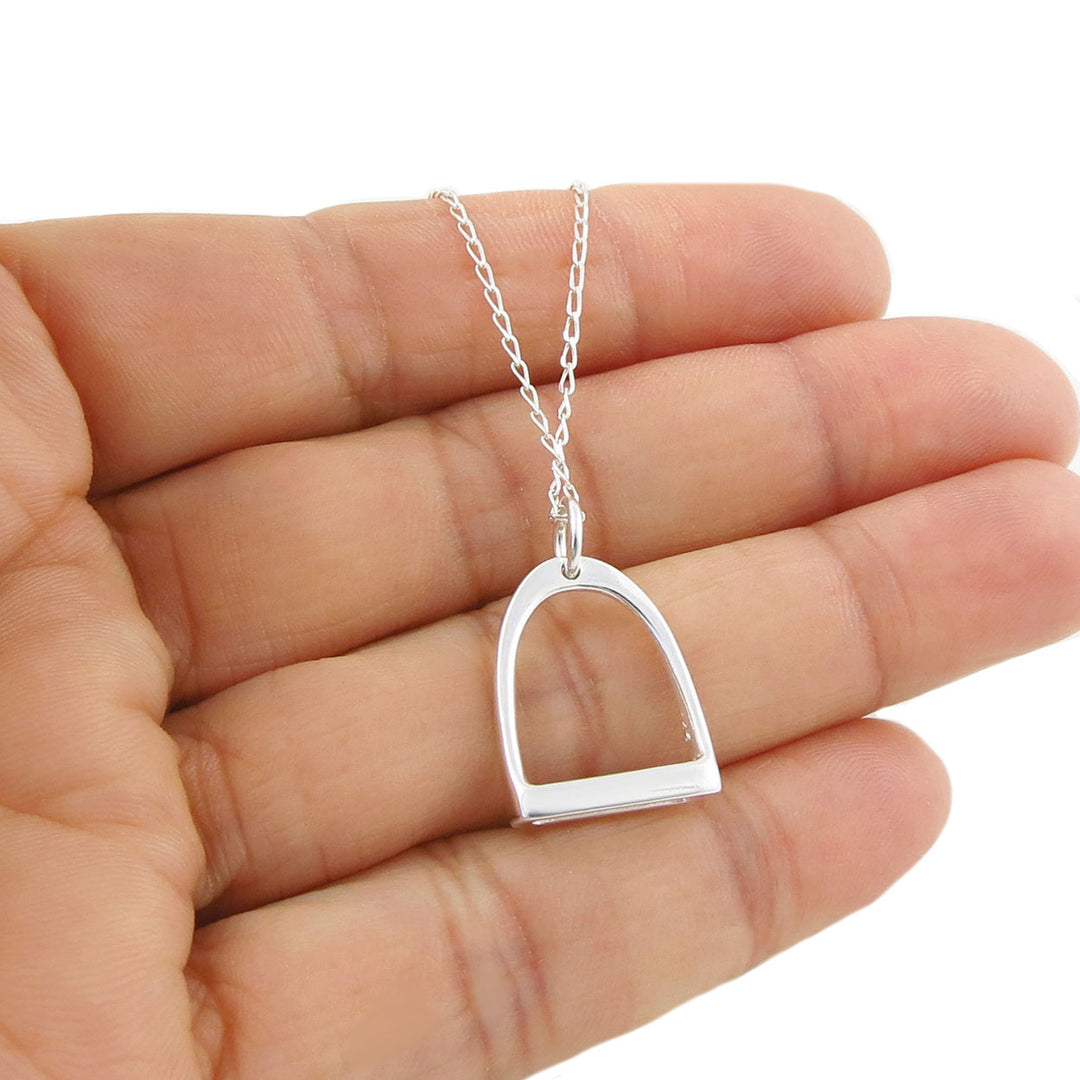  A large equetrian horse stirrup sterling 925 silver pendant and curb chain necklace held in a person's hand