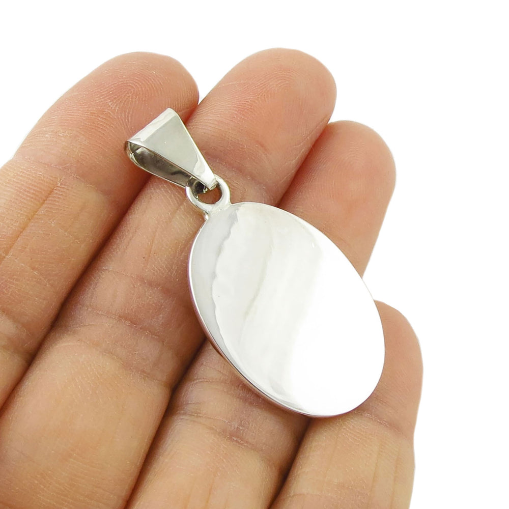A polished sterling 925 silver oval tag pendant jewellery with a reflective surface, held between fingers.