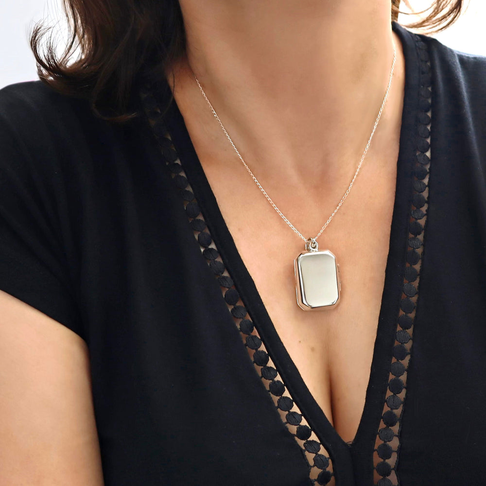 A silver locket style pendant with a hinge opening and a loop for attachment, displayed against a white background.