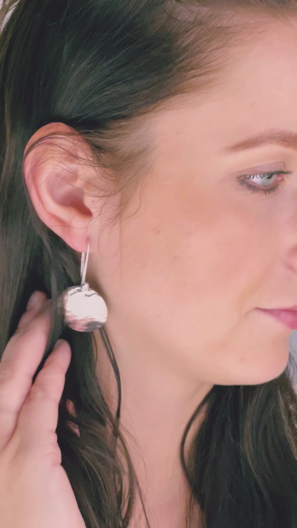 A woman with dark hair modelling a large 925 sterling silver drop earring with a hammered finish 