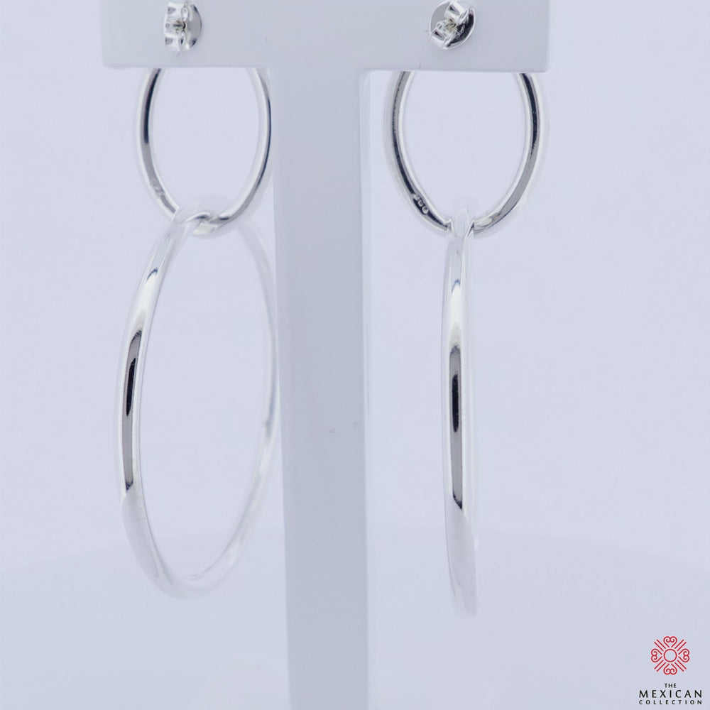 A video of a pair of large double tube hoop earrings revolving on a stand against a neutral background.  