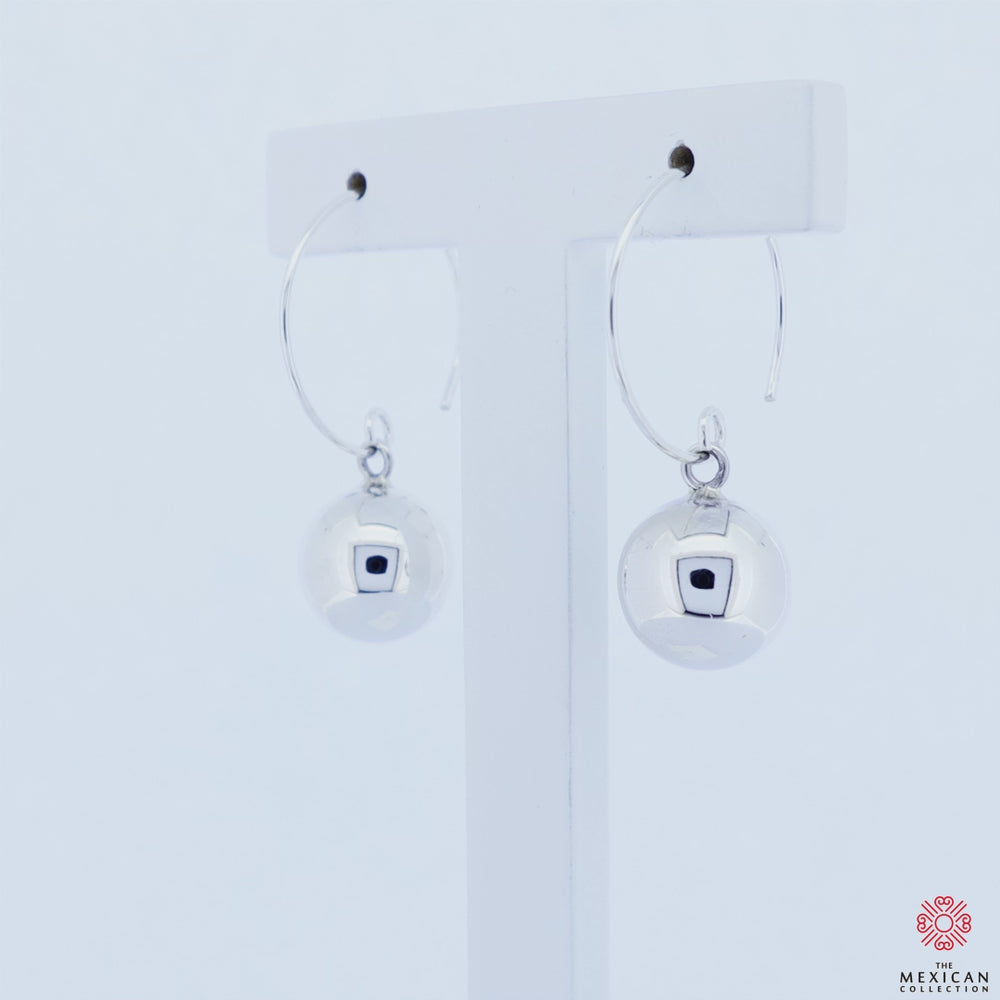 A pair of sterling silver ball earrings with large circle threaders rotating on an earring stand against a white background. 