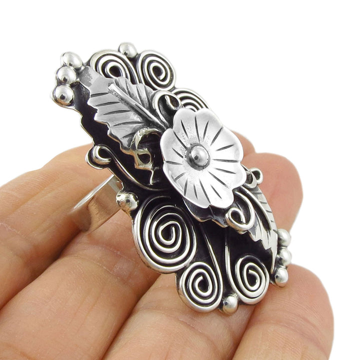 Silver cocktail ring with flower and leaf motis held in a person's hand. 