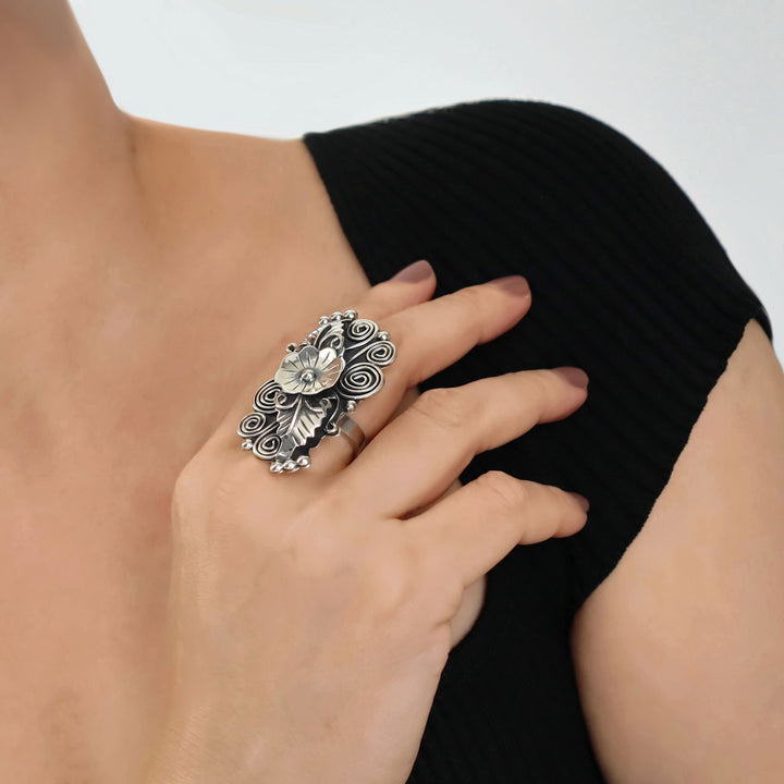 Woman wearing a black top with a large decorative flower and leaf silver cocktail ring.
