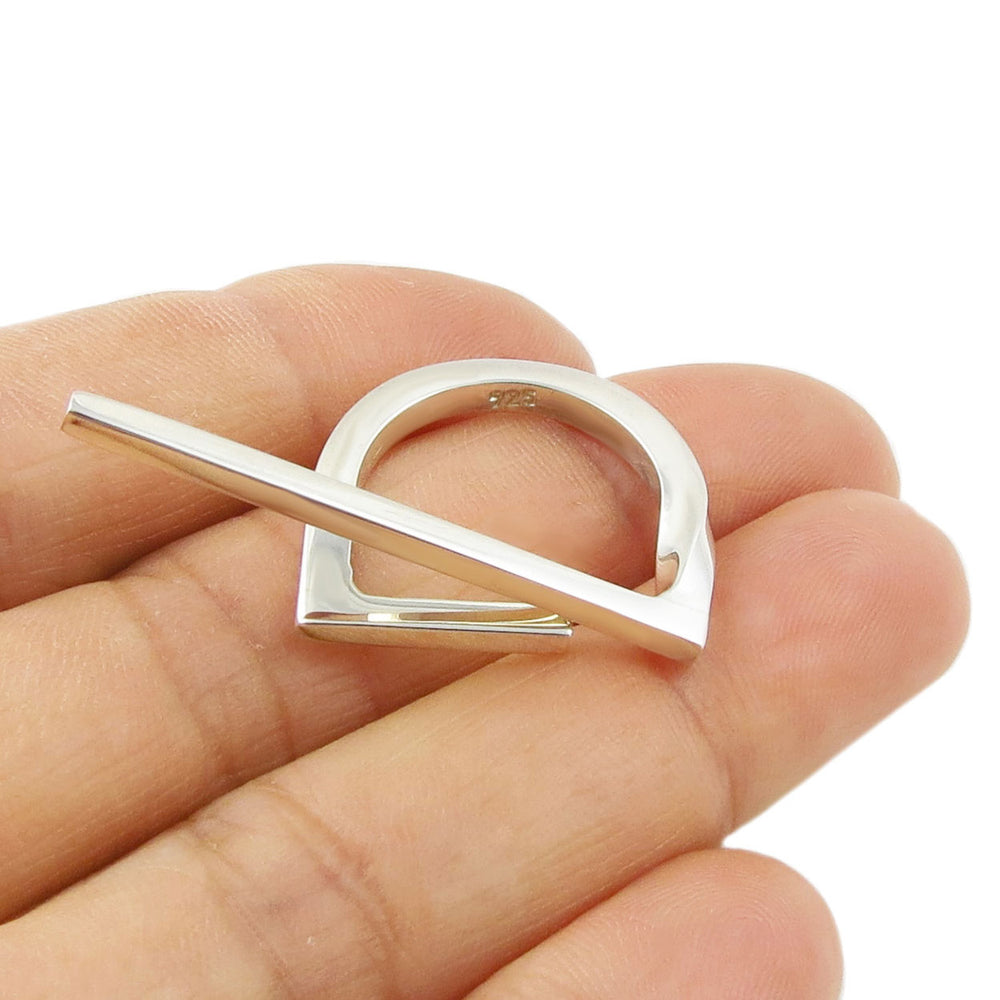 Silver ring with a unique stick design held in a hand against a white background