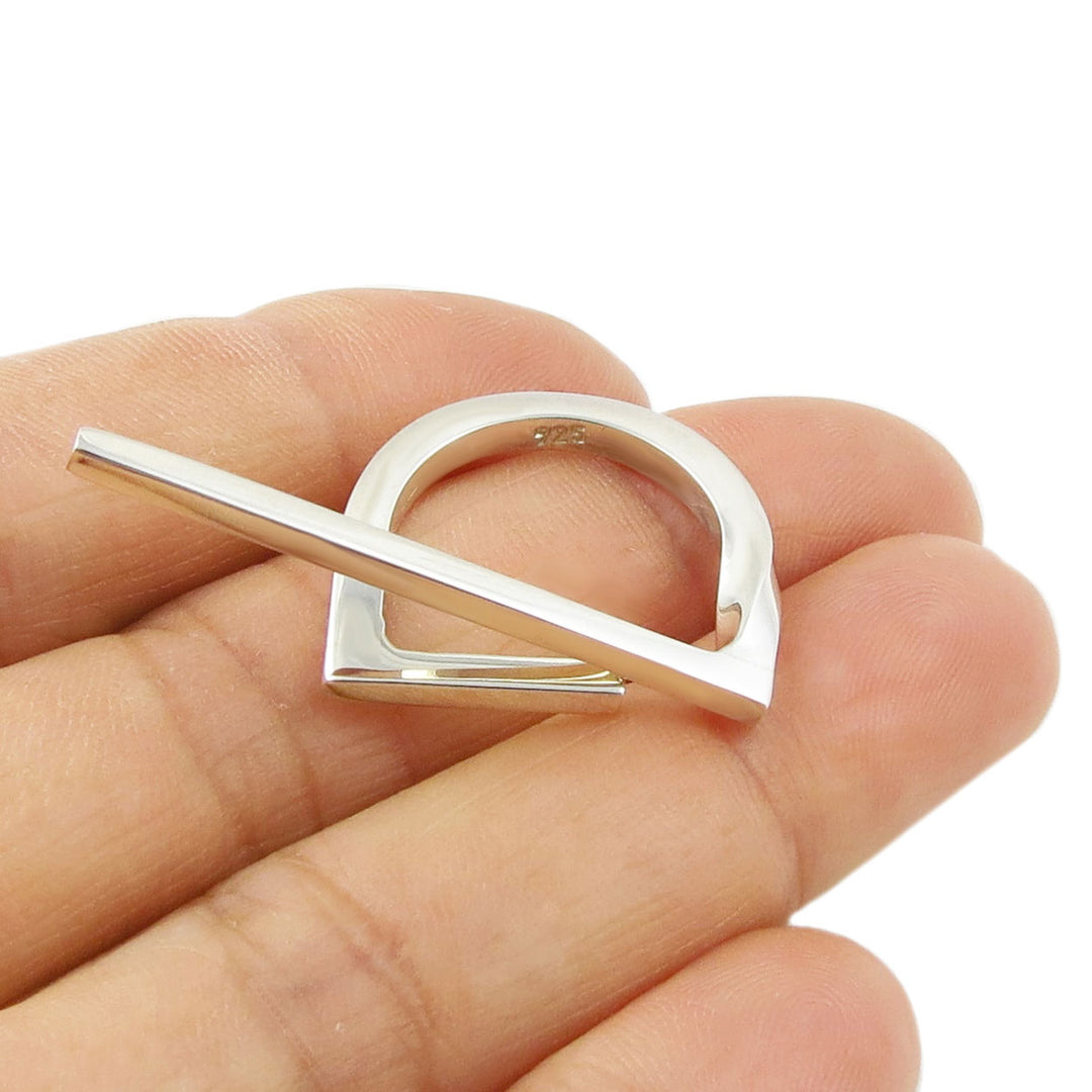 Silver ring with a unique stick design held in a hand against a white background