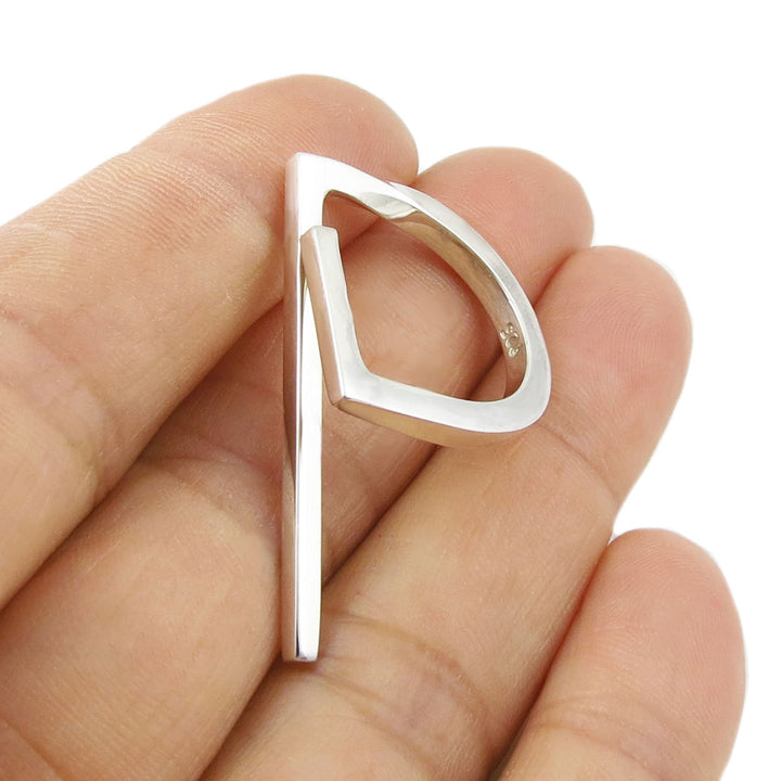 Silver open ring held between fingers against a white background