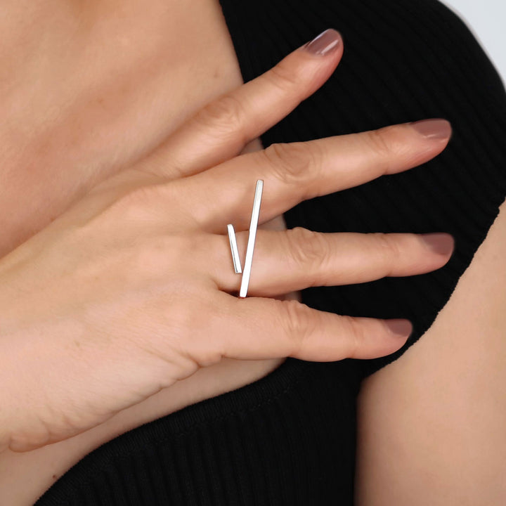 Close-up of a hand wearing a minimalist silver ring on a plain background