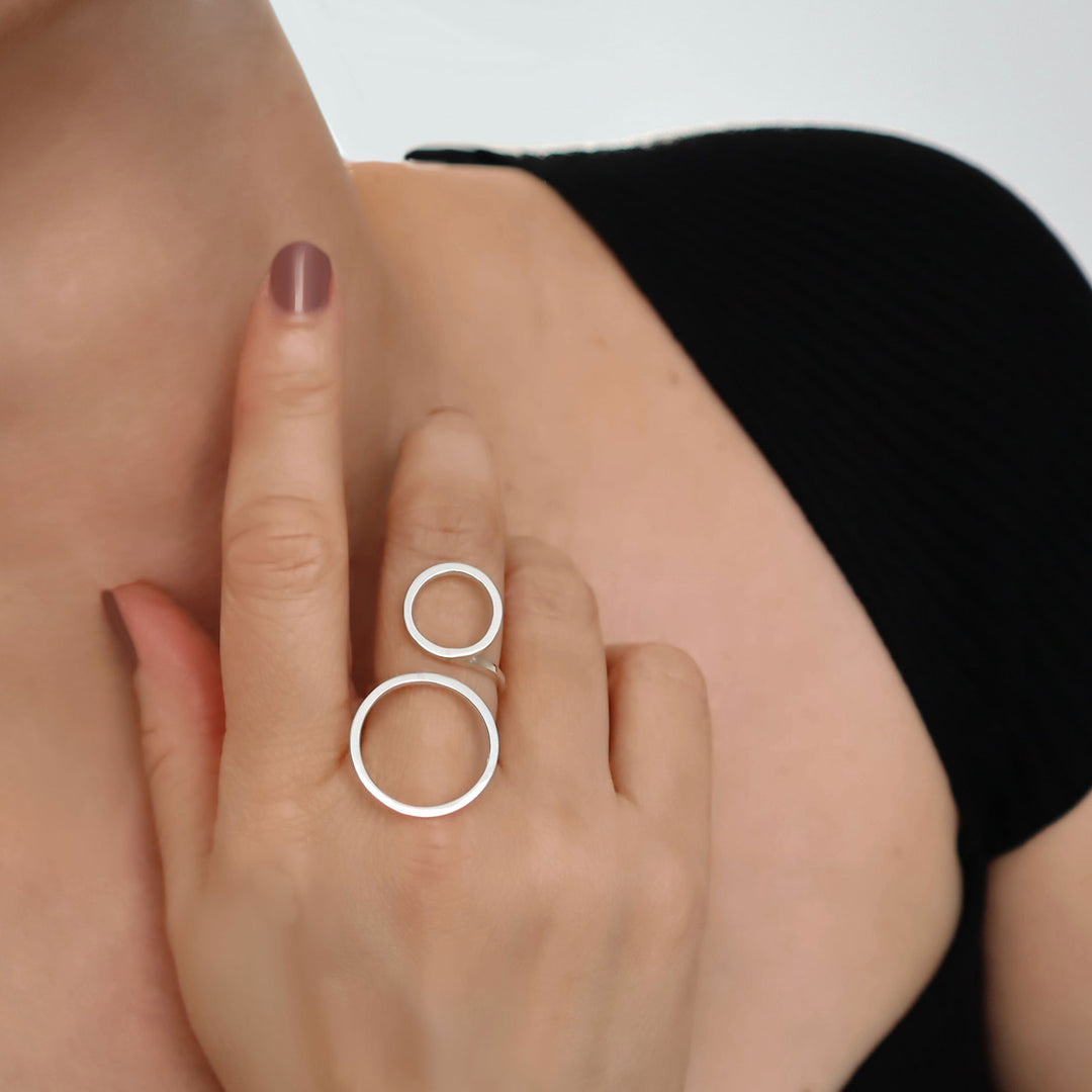 Close-up of a hand wearing a silver ring with two interlocking circles on a neutral background