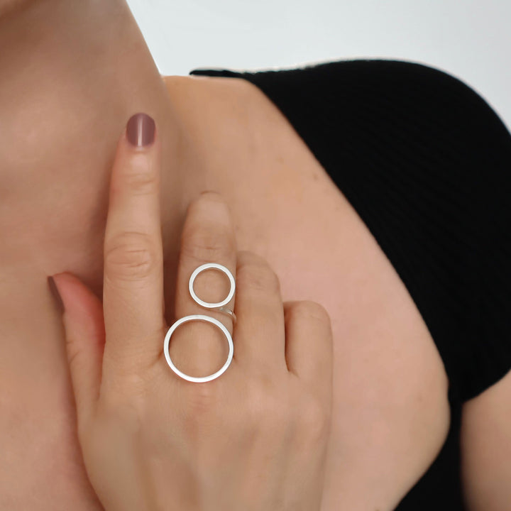 Close-up of a hand wearing a silver ring with two interlocking circles on a neutral background